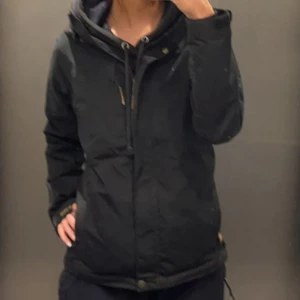 Fjällräven vindjacka - Säljer en svart vinterjacka i mycket bra skick. Den har en praktisk huva och dragkedja framtill. Perfekt för kalla dagar och har en stilren design som passar till det mesta. Jackan är långärmad och har en normal passform.