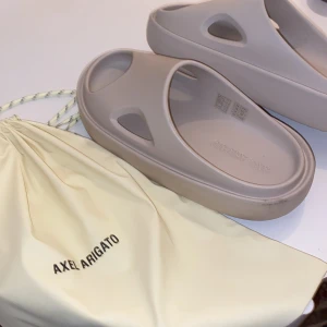 Axel arigato tofflor - AXEL ARIGATO beige magma sandals i storlek 42/43 men passar ändå mig som har på mig st45 skor. Dom är helt nya och bara testade. Adderar 4-5cm till längden, vilket är helt sjukt. En oanvänd Axel arigato påse följer med👍🏾ny pris ligger på runt 2000kr. 