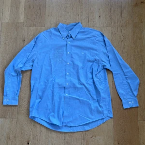 Blå skjorta från Brooks Brothers - Säljer en klassisk blå skjorta från Brooks Brothers i storlek XL. Skjortan är tillverkad i mjuk Supima bomull och har en stilren design med knappar framtill. Perfekt för både vardag och mer formella tillfällen. Den är i mycket bra skick och redo för en ny ägare!