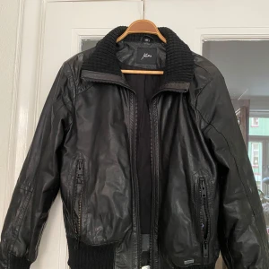 Svart skinnjacka från Jofama - Säljer en snygg svart skinnjacka från Jofama. Den har en cool krage och dragkedja framtill. Perfekt för höst och vår, och den har långa ärmar med ribbade muddar. Jackan är i bra skick och passar perfekt för en casual look.