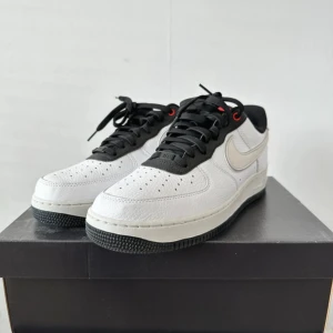 Nike Air Force 1 med broderad fågel - Säljer ett par snygga Nike Air Force 1 i vitt med svart sula och detaljer. Skorna har en cool broderad fågel på sidan och klassisk Nike-logga på hälen. Perfekta för både vardag och fest!
