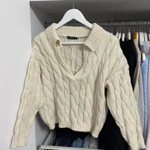 Säljer en superfin beige stickad tröja från Shein. Den har en snygg kabelstickad design och en v-ringad krage som ger en stilren look. Tröjan är croppad, har långa ärmar, perfekt för höst och vinter. Den är i bra skick och passar perfekt till både 