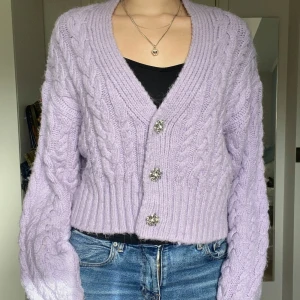 Lila stickad kofta med strassknappar - Kabelstickad kofta från Zara i en ljuslila färg. Stora knappar av strass, finns en extra knapp ifall en skulle lossna! Använd ett fåtal gånger, fint skick