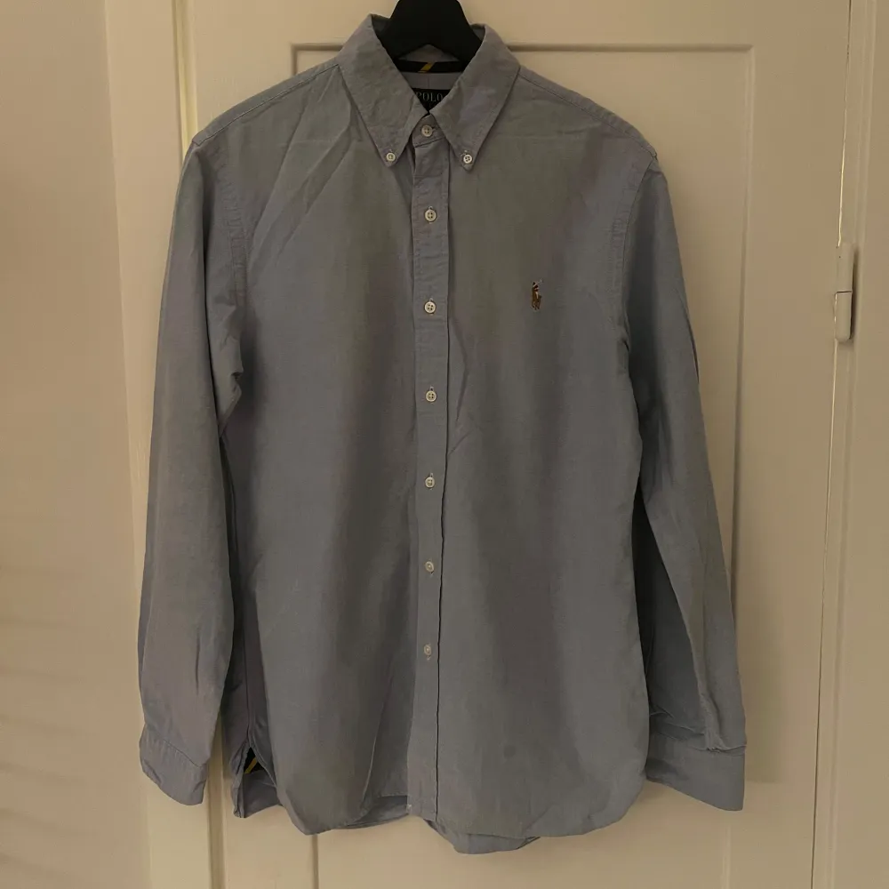 Säljer en stilren blå skjorta från Polo Ralph Lauren i storlek M. Skjortan är slim fit och har långa ärmar med knappar. Perfekt för både vardag och fest!. Skjortor.