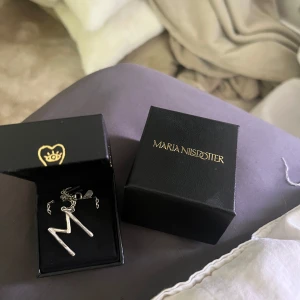 Maria Nilsdotter halsband - Säljer nu mitt fina ”wonky letter necklace” från Maria Nilsdotter. Köpte den i deras butik för ett år sedan o använt det varsamt, inte duschat med det osv. Både bokstaven och kedjan är fin. Skriv för fler bilder💕Längd 50.