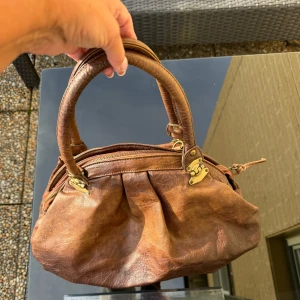 Brun handväska med leopardmönstrat foder - Brun handväska med snygga detaljer i metall. Väskan har ett coolt leopardmönstrat foder och en praktisk dragkedja upptill. Mått -se linjal på bilden. Hämtas på Hägerstensåsen eller ök 🤎