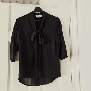 Svart blus från Daisy Grace - Säljer en elegant svart blus från Daisy Grace. Den har trekvartsärmar och en snygg knytning vid halsen som ger en chic touch. Perfekt för både vardag och fest!