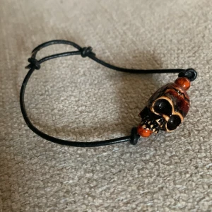 Döskalle armband reglerbart läder  - Snyggt armband med döskalle och orange pärlor på varsin ände.