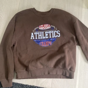 Gina tricot ”Athletics” brun sweatshirt  - Brun, atheltics crewneck från Gina tricot. Original pris= 400kr, finns inte längre. Storlek M. Topp condition, jätte mjuk och håller dig varm. Oversized.