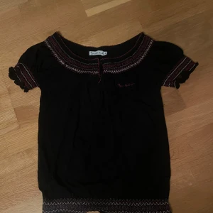 Svart topp från Bondelid - Säljer en svart topp från Bondelid i storlek S. Den har korta ärmar och ett fint mönster med röda och vita broderi-detaljer. 