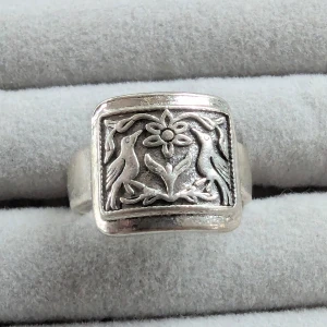 Silverring med fågel- och blommotiv - Unik silverring med ett detaljerat motiv av två fåglar och en blomma. Ringen har en rektangulär platta med intrikata detaljer som ger den en vintagekänsla. Perfekt för dig som vill ha något annorlunda och stilfullt!