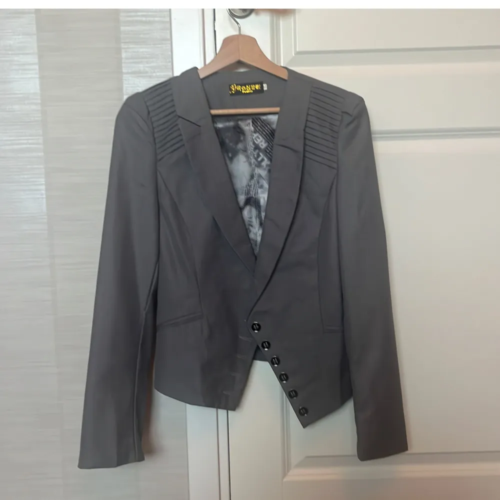 Säljer en stilren grå kavaj som jag har köpt utomlands. Den har en design med ett justerbart bälte i ryggen för perfekt passform! Knapparnas hål har ej sprättats upp och behöver fixas innan användning, men är annars helt funktionell🩷. Takit.