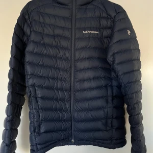 Dunjacka, Peak Performance, MFrost DH, M - Dunjacka från Peak Performance, modell MFrost DH G58685147, mörkblå, storlek M. Jackan är i fint skick.   Material: Ytter 100% polyamid Foder 100% polyamid Fyllning 90% ankdun och 10% ankfjäder.   Mått: Längd ca 70 cm Ärmlängd mätt från axel ca 60 cm