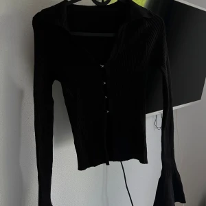 Svart ribbad kofta - Säljer en snygg svart ribbad kofta med långa ärmar och knappar framtill. Perfekt för höst och vinter, den är både stilren och bekväm. Passar till både vardag och fest!