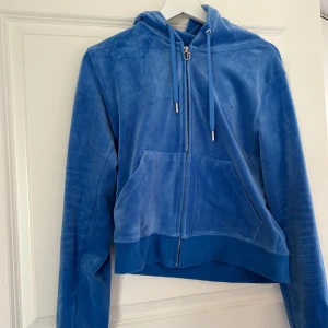 Blå velourjacka från Juicy Couture - Säljer en snygg blå velourjacka från Juicy Couture med dragkedja och huva. Jackan har en avslappnad passform och är perfekt för en casual look. Den har också praktiska fickor framtill. Den är i färgen regatta och original priset för denna är 1300kr. Mycket fint skick, sparsamt använd säljer velourjackan för 700kr. Om man är intresserad av att köpa hela setet, så har jag byxorna i strl L, kan köpas tillsammans med jackan för 1200kr. Vid frågor skriv, jag svarar så fort jag kan!🩷 