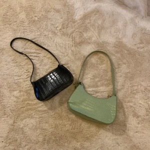 Två axelväskor i krokodilmönster från shein - Säljer två stilrena axelväskor med krokodilmönster. Den ena är svart och den andra är grön. Perfekta för att ge din outfit en trendig touch. Väskorna har en enkel design med en smal axelrem. Endast 50 sek för båda