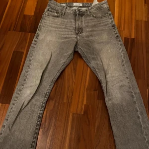 Grå jeansbyxor från Jack and Jones ingår i 4 paket  - Snygga grå jeansbyxor med en klassisk femficksdesign. De har en rak passform och är perfekta för en avslappnad stil. Byxorna har en dragkedja och knapp framtill.