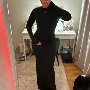 Svart långklänning med öppen rygg - Snygg svart långklänning med en elegant öppen rygg. Klänningen har långa utsvängda ärmar och en tight passform som framhäver figuren. Perfekt för en kväll ute eller en speciell tillställning.