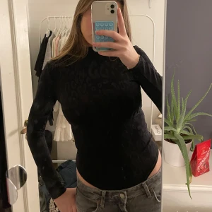 Svart leopardmönstrad body - Säljer en svart långärmad body med leopardmönster. Toppen har en tight passform och är perfekt för en stilren look. Den är tillverkad i ett mjukt och stretchigt material som sitter bekvämt på kroppen.