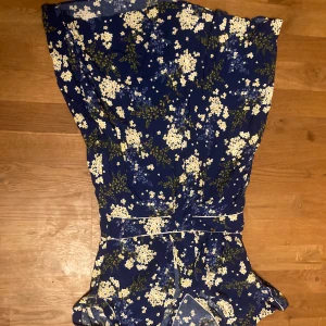 Blommig klänning från Kookai - Säljer en vacker blommig klänning från Kookai i en djup blå färg med vita och gula blommor. Klänningen har en v-ringad hals och korta ärmar. Köpt på second hand fint skick 