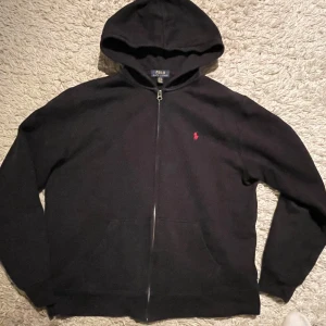 Svart tröja från Polo Ralph Lauren - !!!KÖP VIA POSTNORD!!!Säljer en stilren svart hoodie från Polo Ralph Lauren i väldigt fint skick med dragkedja och den ikoniska röda loggan broderad på bröstet. Storlek xl barn vilket motsvarar S. Vid fler funderingar är det bara att höra av dig! 