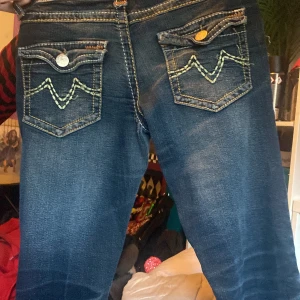 Mörkblå jeans från Diablesse - Snygga mörkblå jeans från Diablesse med unika bakfickor dekorerade med kontrasterande sömmar. Jeansen har en klassisk femficksdesign och knappar med märkets logga 