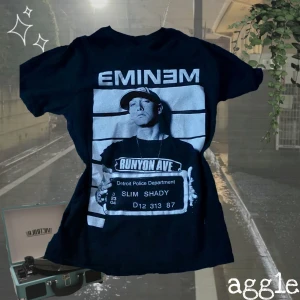 Svart Eminem t-shirt - Cool svart t-shirt med Eminem-tryck på framsidan av Eminem med texten 'Runyon Ave' och 'Slim Shady'. Perfekt för fans av rap och streetwear. Köpt på Camden market, säljer då den inte kommer till användning. Använd ett fåtal gånger.