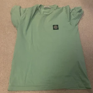Grön Stone Island T-shirt - Säljer en snygg grön Stone Island T-shirt  Har två små hål på ryggen  Pris kan diskuteras 