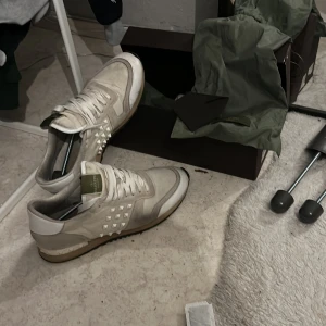 Valentino Rockrunners  - Snygga Valentino sneakers i beige och vita. Skorna är inte sönder eller så, väldigt bra skick på dom. De är bara lite smutsiga av snö men jag fixar rent dom innan jag fraktar såklart! Alla nitar är kvar och inget är sönder! Perfekta för att ge din outfit en lyxig touch. Det är bara att höra av sig eller lägga ett bud om man är intresserad, så tar vi de därifrån!