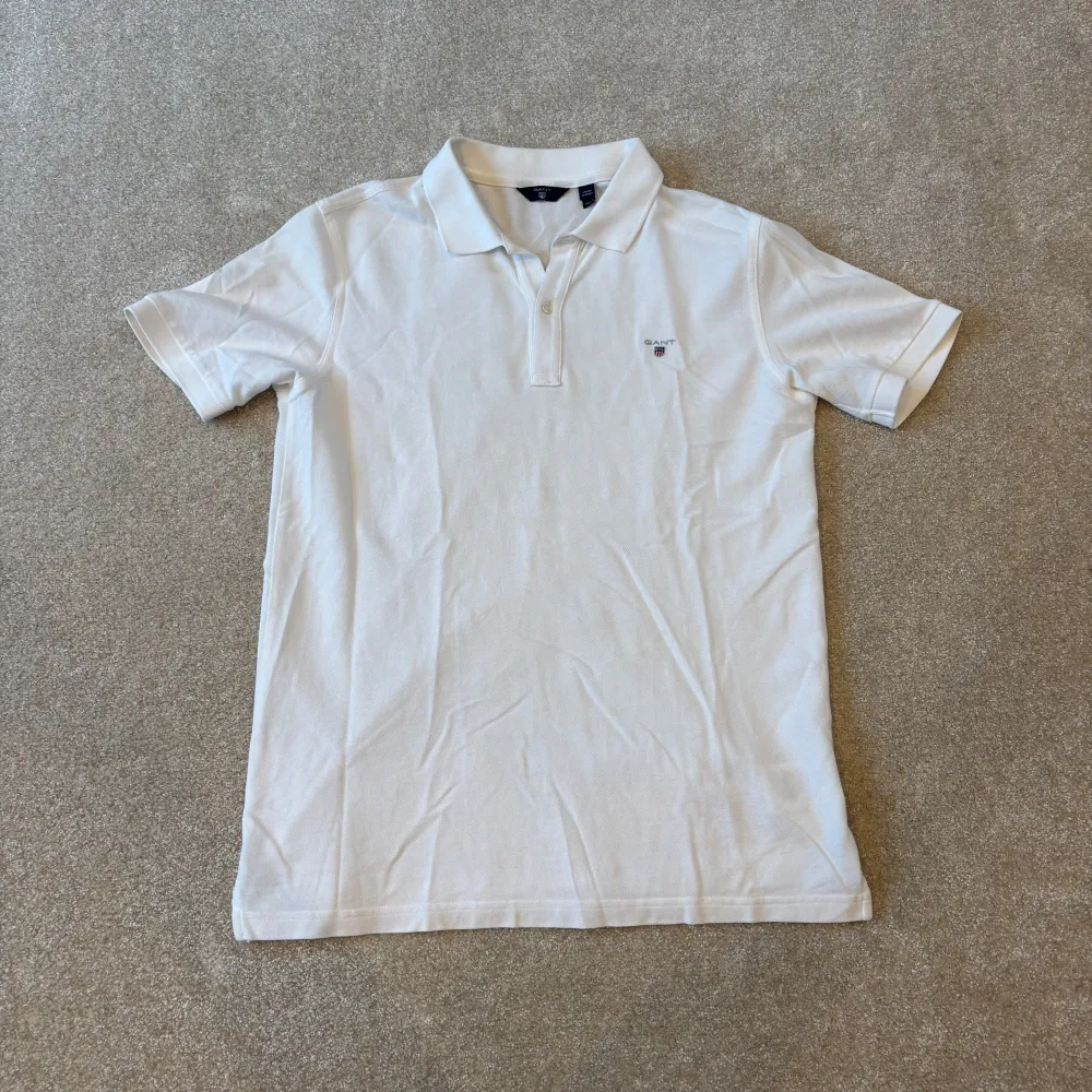 Säljer en klassisk vit pikétröja från gant med krage och korta ärmar. Perfekt för en stilren och avslappnad look. Tröjan har en liten logga på bröstet och är tillverkad i ett bekvämt material.. Paidat.