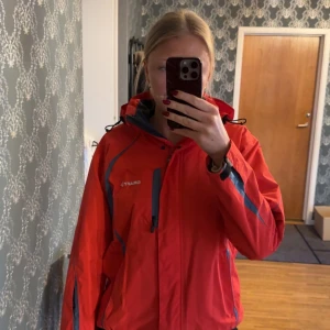 Röd vindjacka från Craft - Säljer en röd vindjacka från Craft med huva och dragkedja.  Perfekt för att hålla dig bekväm och skyddad mot väder och vind. Storlek 42 men sitter som 40. Sparsamt använd så i gott skick. 