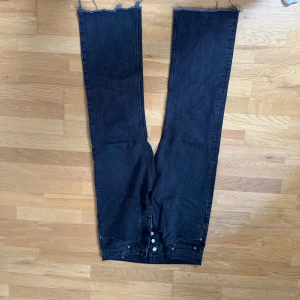 Svarta jeans från Hope - Snygga svarta jeans från Hope med råa kanter och en klassisk femficksdesign. De har en rak passform och är perfekta för en avslappnad stil. Jeansen har en knappgylf och är tillverkade i ett slitstarkt material. 31