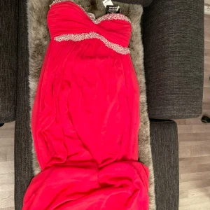 Röd axelbandslös klänning med pärlor - Säljer en fantastisk röd axelbandslös klänning från Pronovias. Klänningen har vackra pärldetaljer längs bysten och en elegant, flytande design. Perfekt för speciella tillfällen! 💃KÖPAREN betalar frakten.