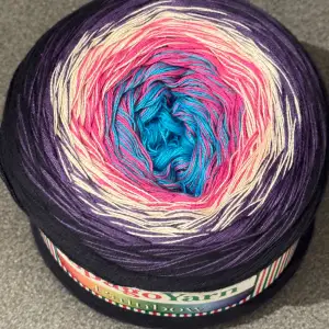 Säljer ett nystan flerfärgat garn från SpagoYarn. Garnet har en vacker gradient av blått, rosa, lila och beige. Det är 55% bomull och 45% akryl, väger 250 g med en längd på 1000 m. Perfekt för kreativa stick- och virkprojekt!