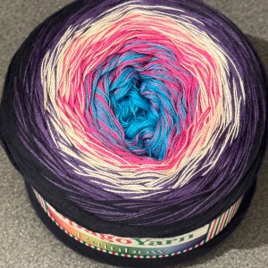 Flerfärgat garn från SpagoYarn - Säljer ett nystan flerfärgat garn från SpagoYarn. Garnet har en vacker gradient av blått, rosa, lila och beige. Det är 55% bomull och 45% akryl, väger 250 g med en längd på 1000 m. Perfekt för kreativa stick- och virkprojekt!