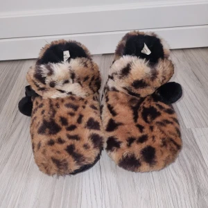 Leopardmönstrade tofflor från River Island - Mysiga tofflor med leopardmönster från River Island. De är täckta i mjuk pälsimitation och har en bekväm passform. Perfekta för att hålla fötterna varma och stiliga hemma.