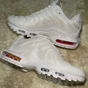 Vita Nike Air Max Plus - Säljer ett par stilrena vita Nike Air Max Plus med den ikoniska Tuned Air-dämpningen. Skorna har en snygg vågig design och synliga luftkuddar i sulan för extra komfort. Perfekta för dig som vill ha en sportig look med en touch av retro.