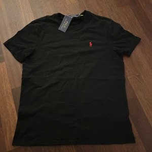 Svart t-shirt Polo Ralph Lauren - Snygg svart t-shirt från Polo Ralph Lauren med  klassiska röda logotypbroderiet. Gjord i mjuk bomull. Storlek M