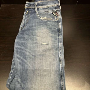 Blå jeans från Replay - Snygga blå Replay Hyperflex jeans i modellen Anbass. De har en klassisk femficksdesign med dragkedja och knapp. Perfekta för en stilren look med en bekväm passform.