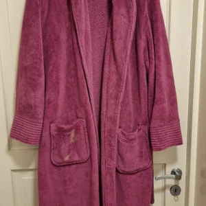 Rosa morgonrock från Miomare - Säljer en mysig rosa morgonrock från Miomare. Den har långa ärmar och två praktiska fickor framtill. Materialet är 100% polyester vilket gör den mjuk och bekväm. Perfekt för att hålla sig varm och skön hemma.