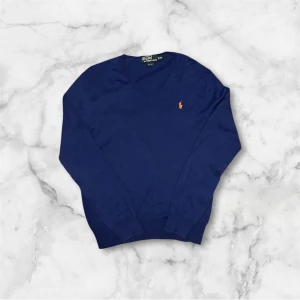 Blå tröja från Polo Ralph Lauren - Säljer en stilren blå tröja från Polo Ralph Lauren med v-ringning och det klassiska logotypbroderiet i orange på bröstet. Tröjan har en slim passform och är perfekt för en elegant look. 10/10 skick