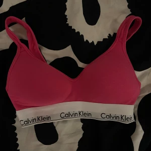 Rosa linnetopp från Calvin Klein - Säljer en snygg rosa linnetopp från Calvin Klein med elastiskt band och logga under bysten. Perfekt för en avslappnad stil. Toppen har breda axelband och är tillverkad i mjukt material.