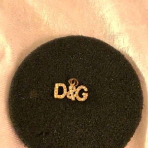 Guldigt D&G hänge med strass - Elegant hänge från Dolce & Gabbana i guld med glittrande strassdetaljer. Perfekt för att ge en lyxig touch till ditt halsband.