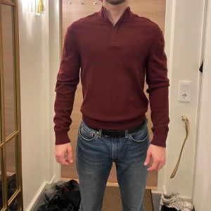 Vinröd tröja från BOSS - Säljer en stilren vinröd tröja från BOSS i bomull och ull. Tröjan har en dragkedja vid halsen och långa ärmar. Perfekt för en snygg och bekväm look.