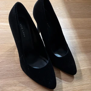 Svarta pumps från New Look - Eleganta svarta pumps från New Look i sammet med spetsig tå och klack. Perfekta för en stilren look. Klack ca 11 cm. 