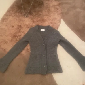 Grå kofta från Wera - Mysig grå kofta populär kofta från Wera med knappar framtill och stora fickor. Perfekt för kyliga dagar med sin stickade design och långa ärmar. En stilren och bekväm tröja för alla tillfällen.Köpt på Vinted, men tidigare ägaren har tvättat denna så den krympt. Står xs men är nu liten i storleken. Pris är därför diskuterbart.