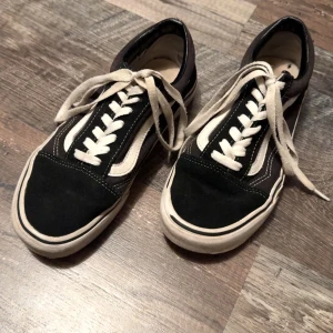 Svarta sneakers från Vans - Säljer ett par klassiska svarta Vans sneakers med vit sula och snörning. Skorna har den ikoniska vita sidostripen och är perfekta för en avslappnad stil.