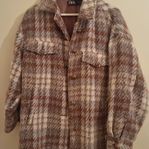 Rutig overshirt från Zara - Snygg rutig overshirt från Zara i bruna och vita toner. Jackan har långa ärmar och knappar framtill samt två bröstfickor med lock. Perfekt för lager-på-lager-stil under kyligare dagar.