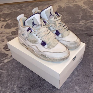 Nike Air Jordans Purple Metallic - Säljer ett par klassiska Nike Air Jordans i vitt med lila detaljer. Skorna har snörning och den ikoniska Jumpman-loggan på tungan och hälen. Perfekta för sneakerheads som vill ha en stilren look.