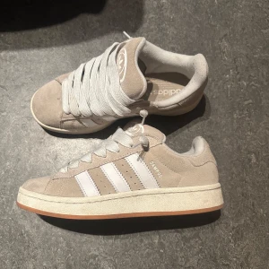 Beige Adidas Campus sneakers - Snygga beige Adidas Campus sneakers med klassiska vita ränder och gummisula. Skorna har snörning och är tillverkade i mocka för en stilren look. Pris kan diskuteras vid snabb affär